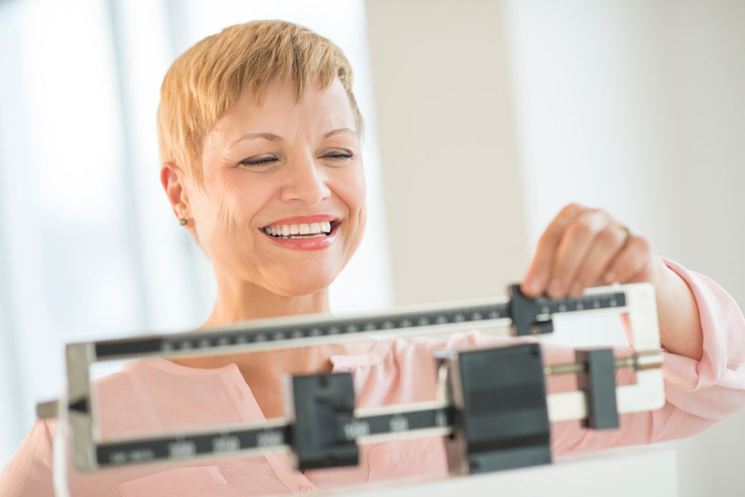 Happy woman weighing herself on a scale and wondering "Can collagen peptides cause weight gain?"