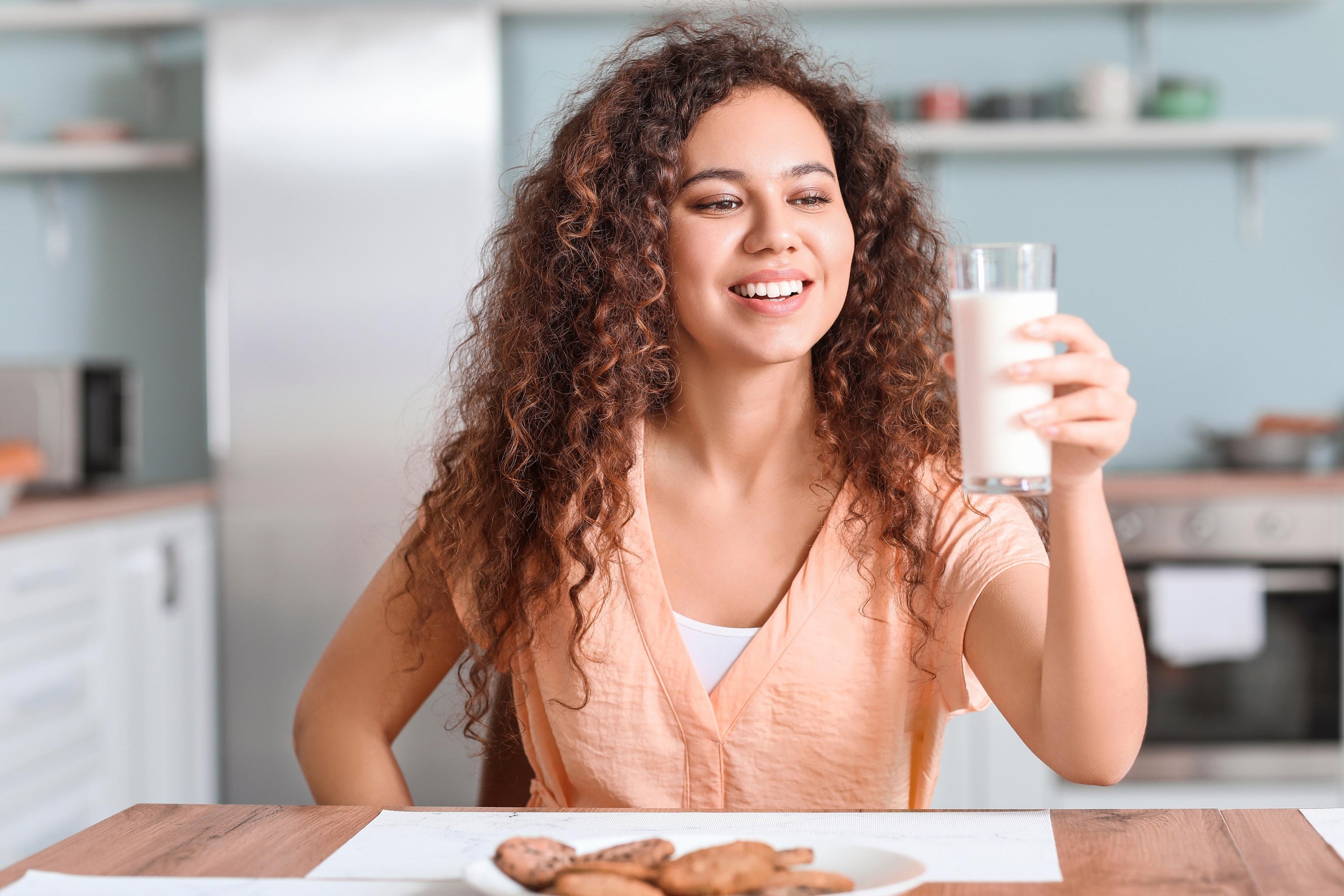 Curly-haired woman holding a glass of collagen for breakfast, which is the schedule that she finds to be the best time to take collagen