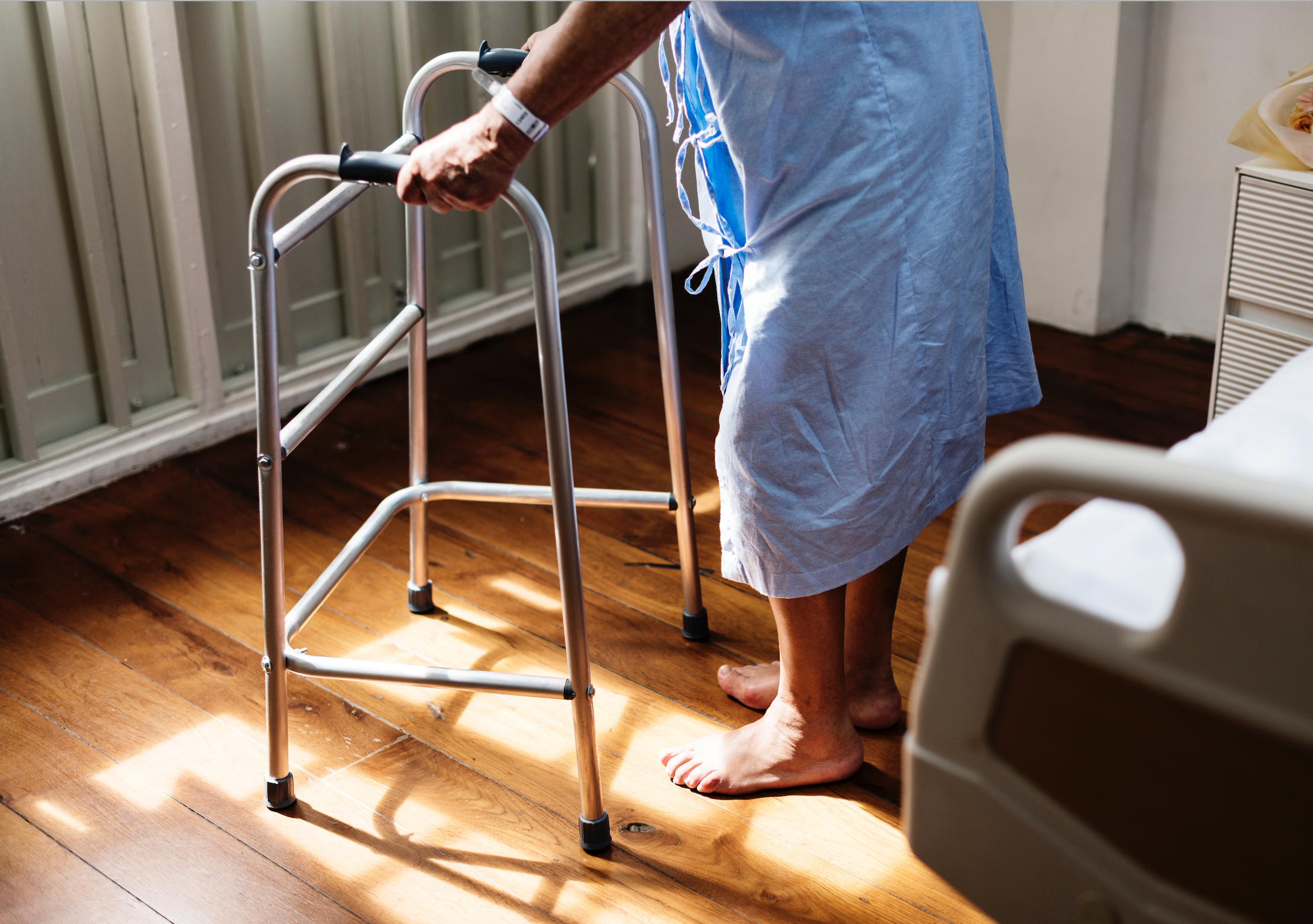 Man in a blue hospital gown is standing with the help of a walker to prevent new sore formation, which speeds up pressure ulcer treatment