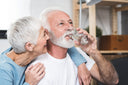 Smiling wife looking at her husband taking tiny sips of water to supplement his diet after gastric bypass
