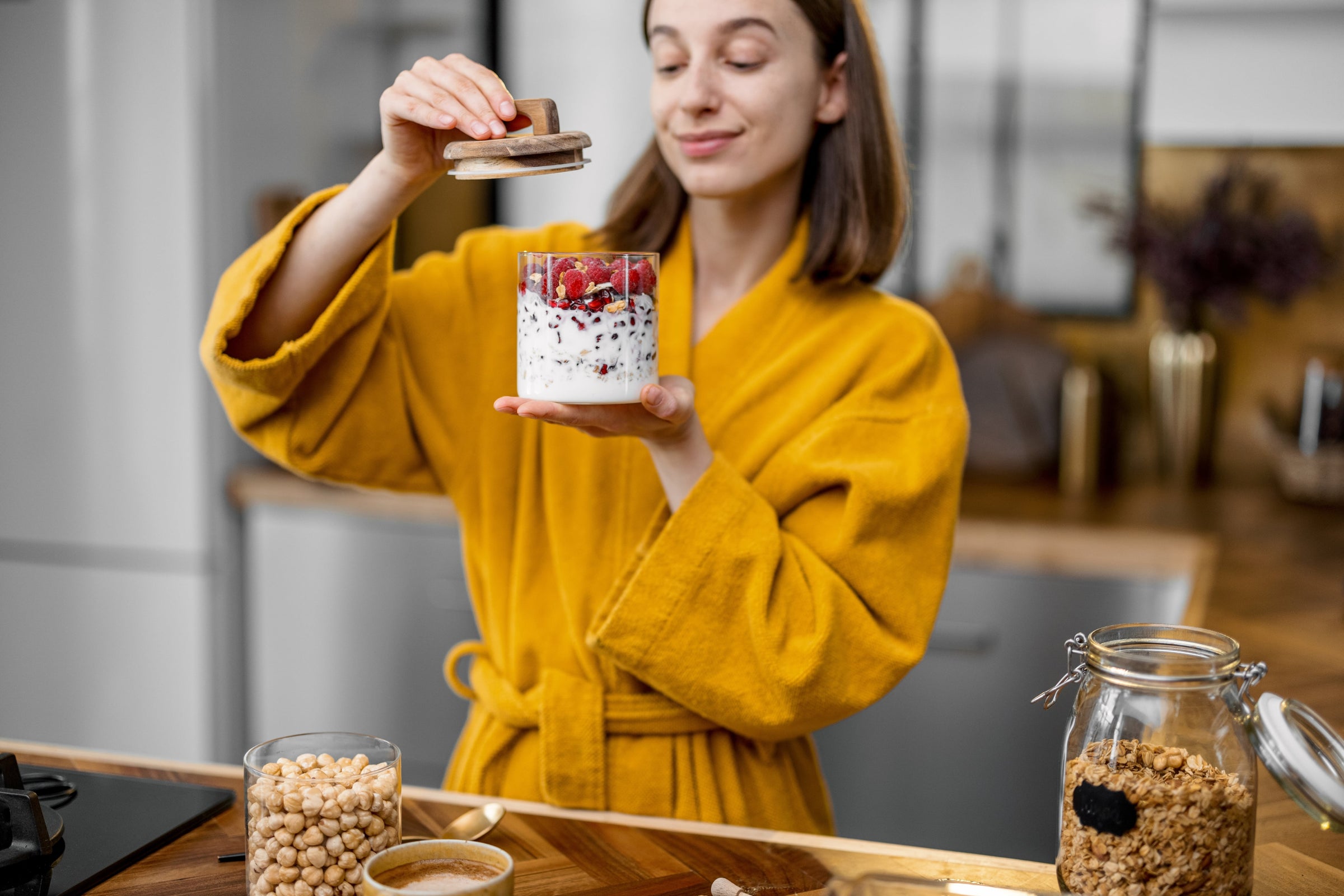 Young woman in yellow bathrobe holding a glass of raspberry yogurt with collagen peptides