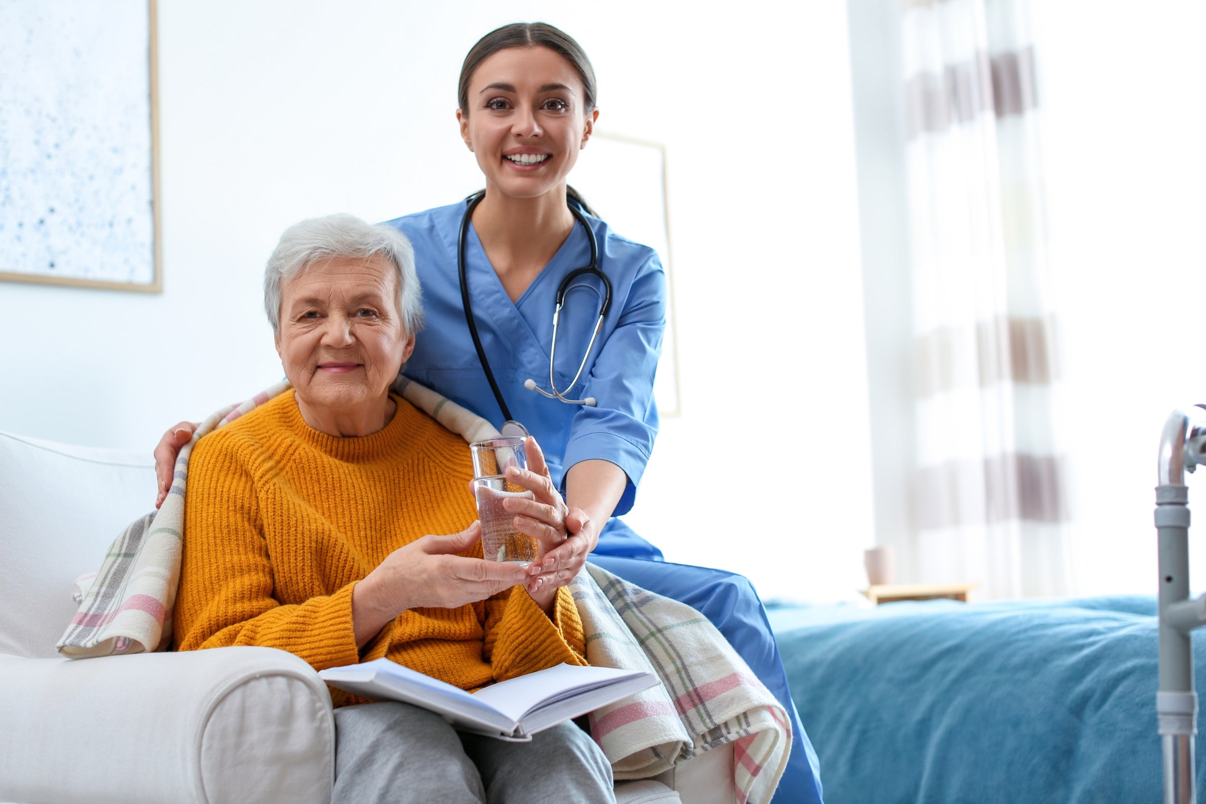 Nurse in a geriatric hospital giving water to an elderly woman so she stays hydrated—a significant factor in how nutrition affects pressure ulcers