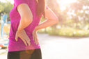 Woman standing while holding her lower back, which is the location of her hip pain