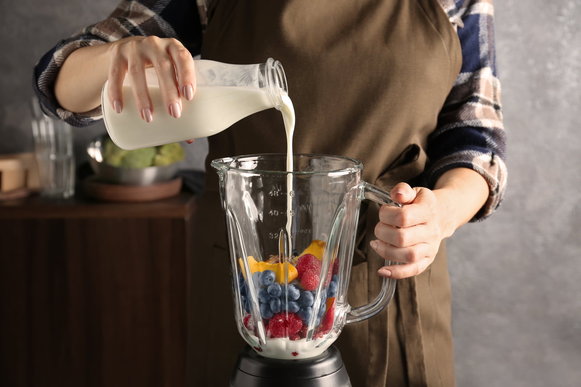 Woman pouring nano-hydrolyzed liquid collagen, one of the supplements to help lose weight, into a blender filled with colorful fruits