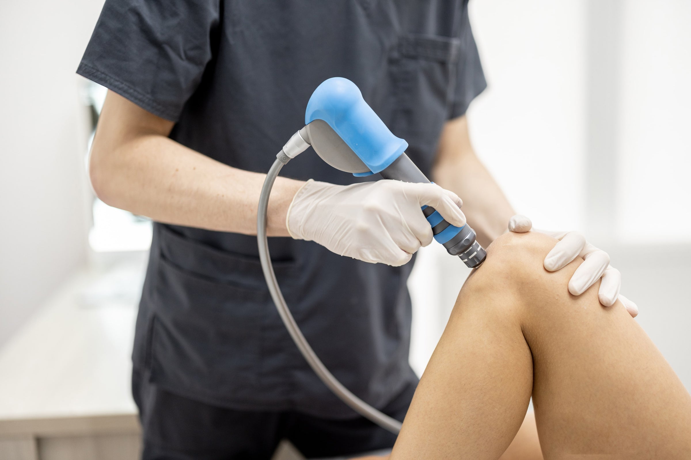 Doctor applies shock wave therapy on the knee of a patient experiencing one of the 6 types of knee pain 