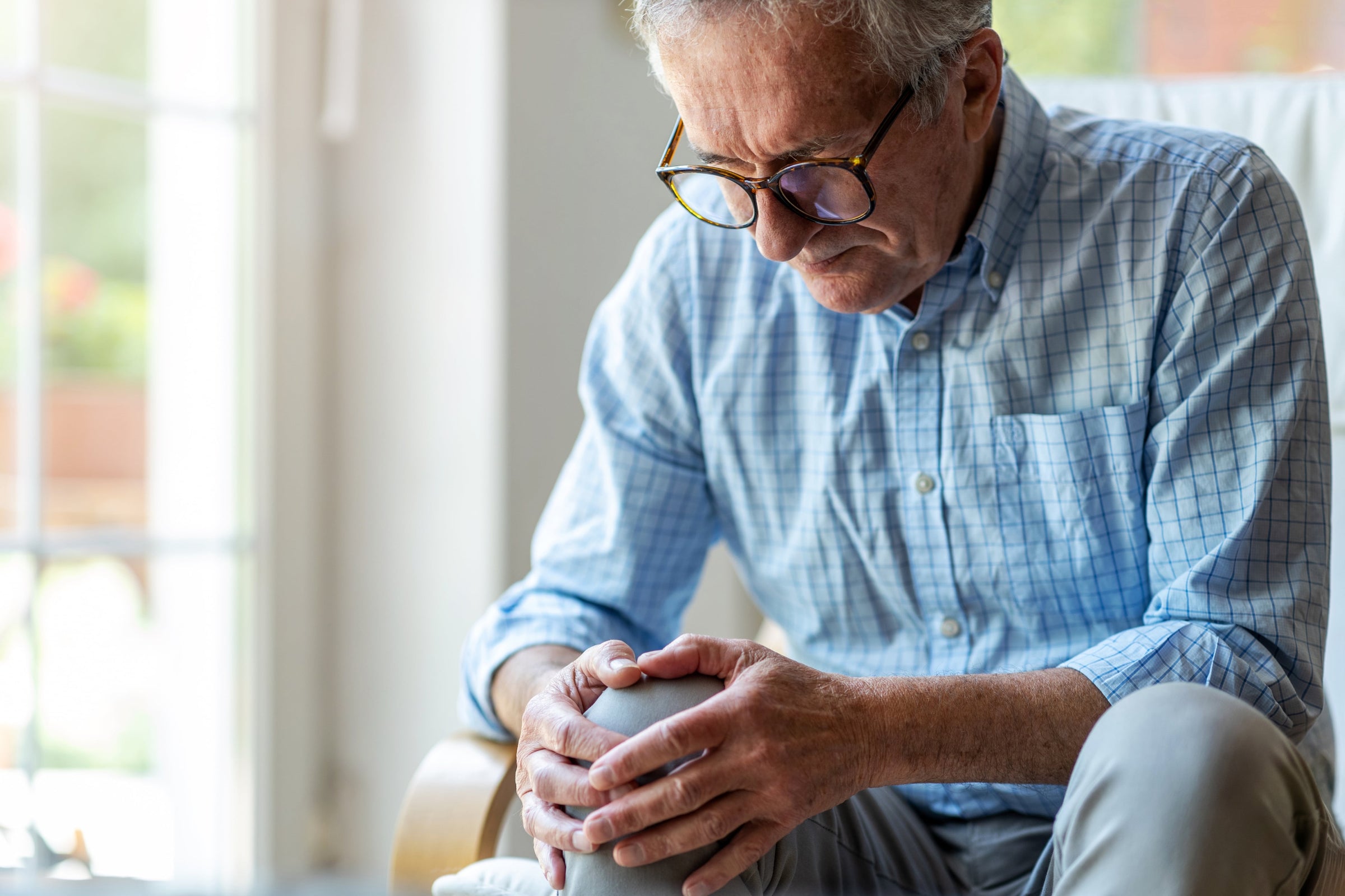 Senior man clutching his painful knee while wondering, "What can cause knee pain without injury?"