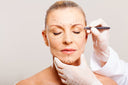Doctor's hands wearing gloves drawing correction lines on a woman's face while giving her tips about the plastic surgery recovery process