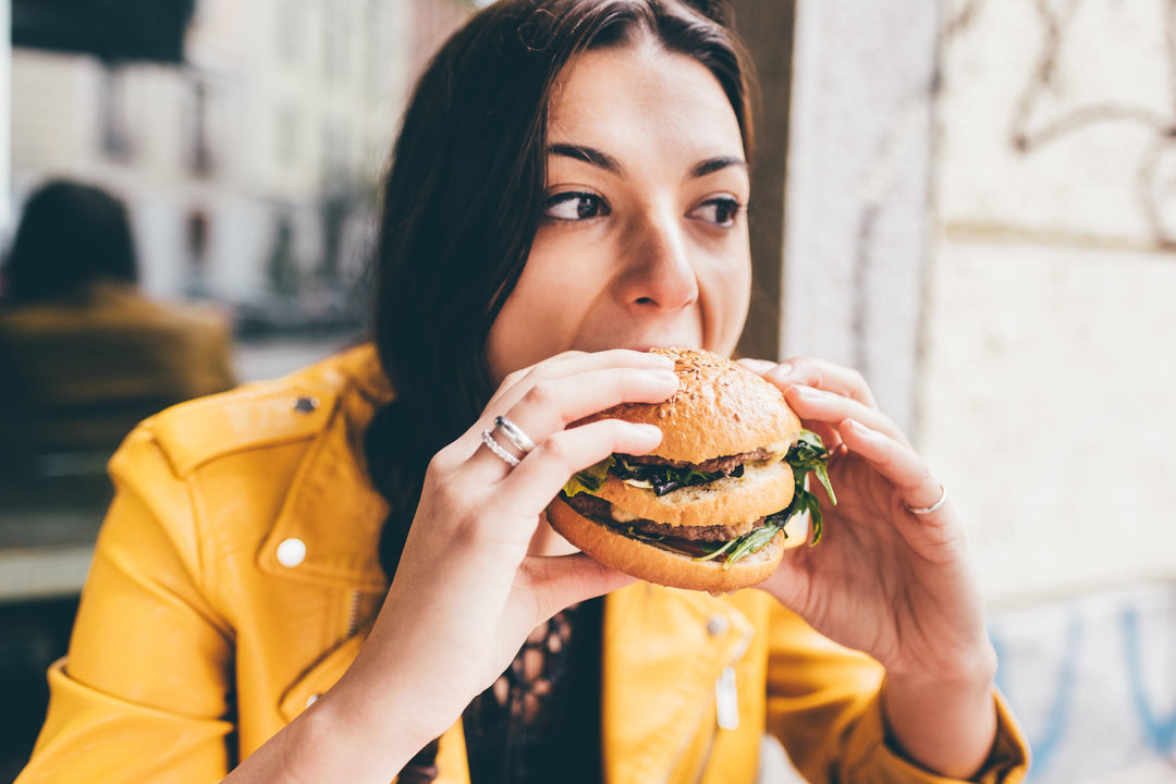 Young woman eating an unhealthy hamburger, which is one of the slow healing wounds causes